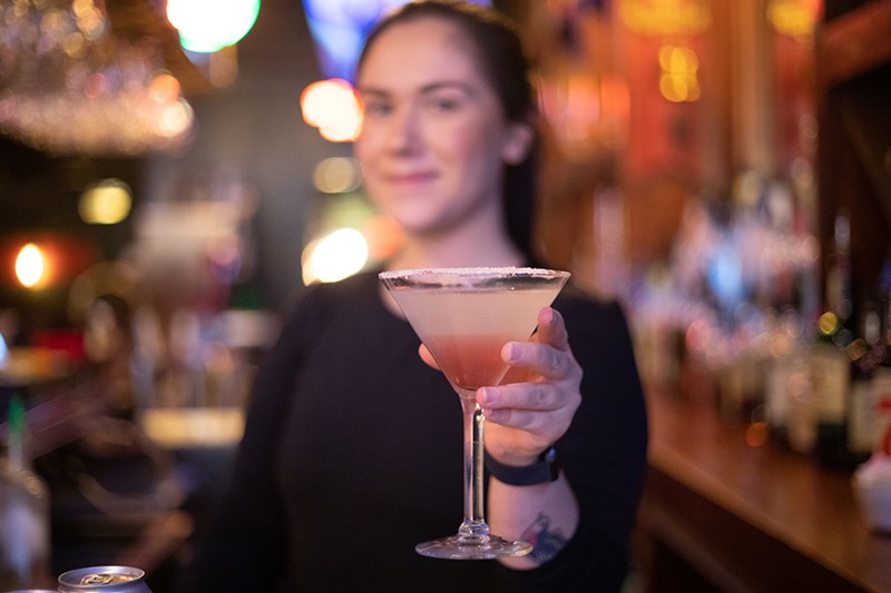 A bartender holds out a martini to the viewer.