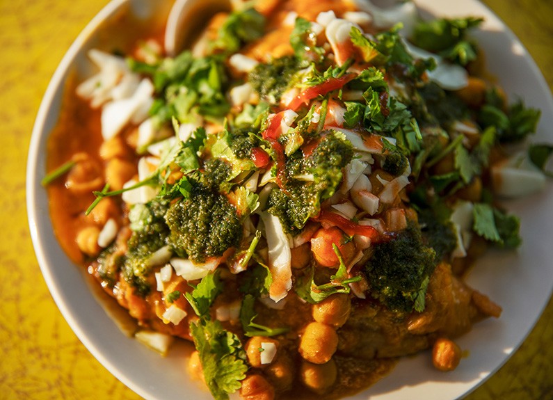 The samosa chaat is made with two samosas filled with spiced potatoes and peas then topped with shredded cabbage, onion, cilantro, chana masala, greens and tamarind chutney. - ZACHARY LINHARES