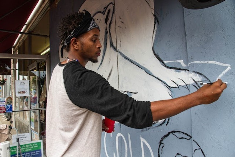 Artist Cornell McKay paints a polar bear on the plywood covering Plowsharing Crafts. - COURTESY OF PAINTING FOR PEACE IN FERGUSON, A CHILDREN'S BOOK