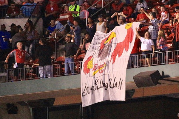 Protesters unfurled a banner of a Cardinals mascot wearing a jersey that says "Expect Us" and holding a "Racism Lives Here" sign. - Used with permission