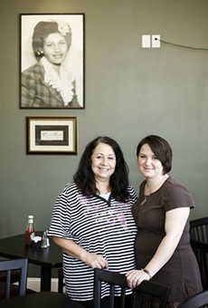 Mary Samuelson (left) and daughter Amy Keller (right) stand beneath a portrait of the restaurant's namesake.