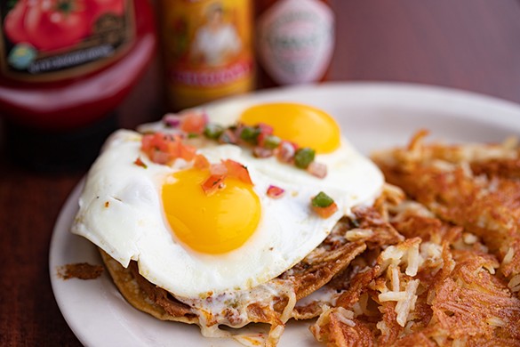 NachoStada with a double-layered tostada, chorizo, refried beans, green chili salsa, queso, two sunny-side-up eggs and pico.