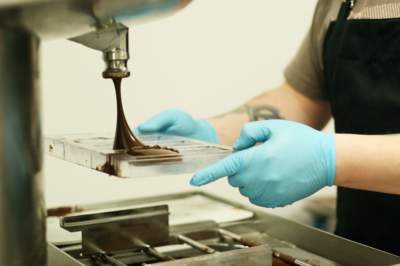 With a warmed mold in his hands, chocolate-maker Alan McClure passes it through the cascading chocolate, making sure to get the right amount in each bar impression.